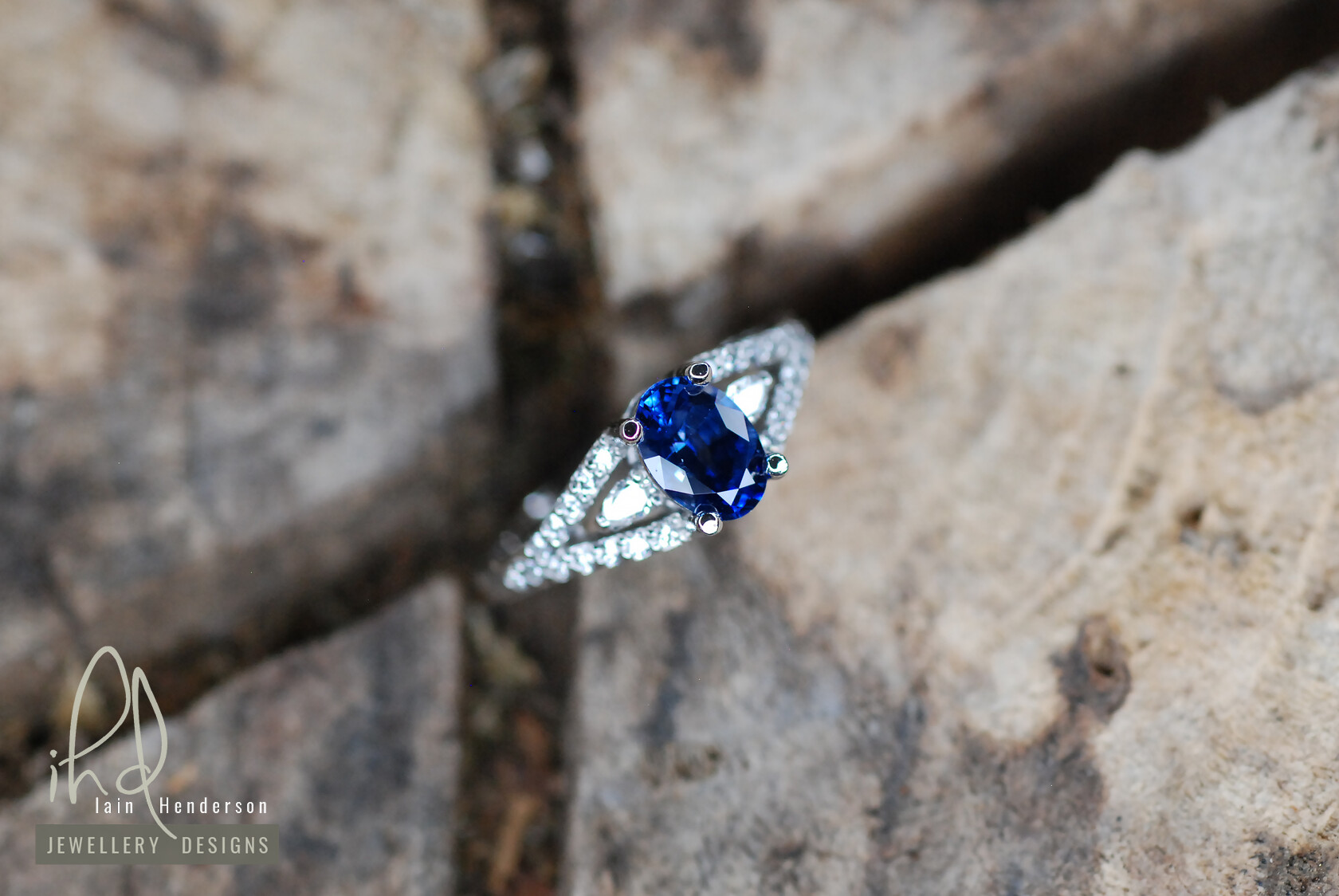 Bespoke platinum engagement ring with an oval sapphire centre stone, small pear shaped diamonds between the split shank and small diamonds on the shoulders